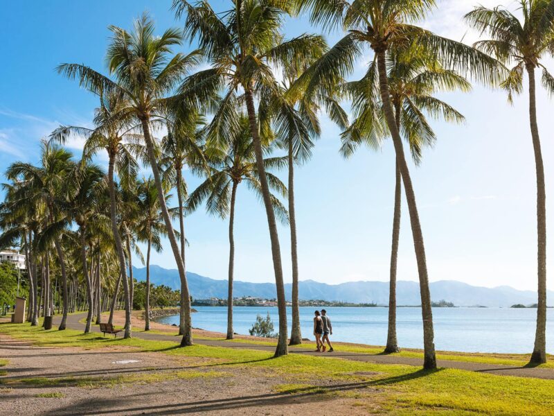 Photo de la Promenade Pierre Vernier au bord de l'eau à Nouméa. On y voit 2 personnes marcher le long d'un sentier au bord de la mer.