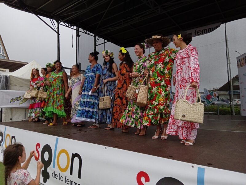 Photo prise sur l'estrade du Salon de la Femme 2023 en Nouvelle-Calédonie. On y voit 11 femmes alignées portant des créations artisanales (robes, sacs à main, couronnes de fleurs et chapeaux).