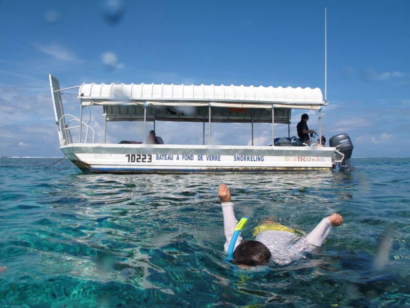 Photo du bateau à fond de verre de Ouest Corail. Un enfant faisant du snorkeling à Bourail est visible au premier plan. 