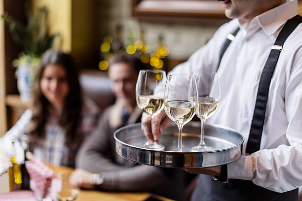 Travailler dans un hôtel de luxe : food and beverage attendant servant du vin blanc avec élégance au restaurant d'un hôtel de luxe